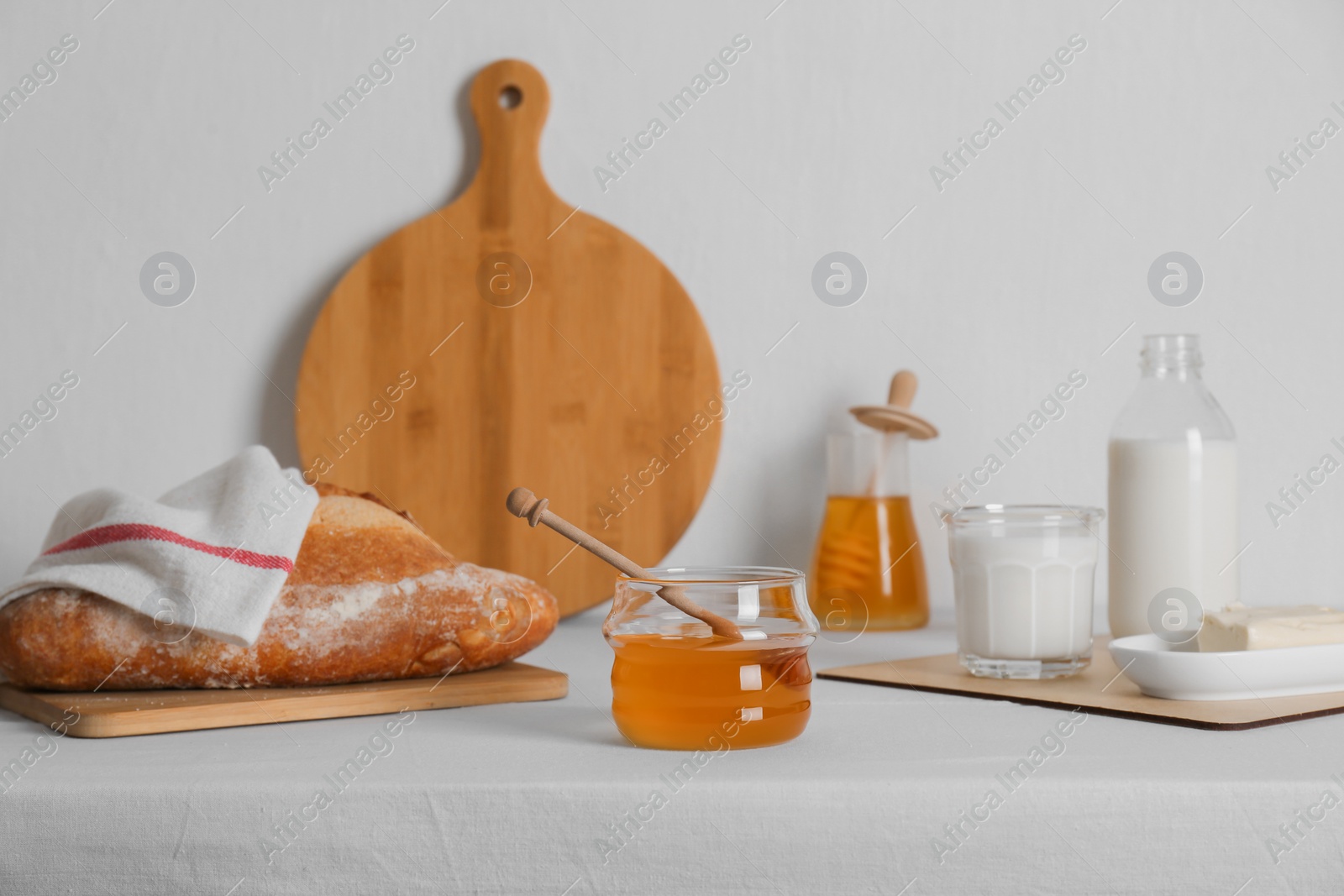 Photo of Jar with honey, milk, butter and bread served for breakfast on table indoors