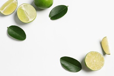 Fresh ripe limes and leaves on white background, flat lay. Space for text