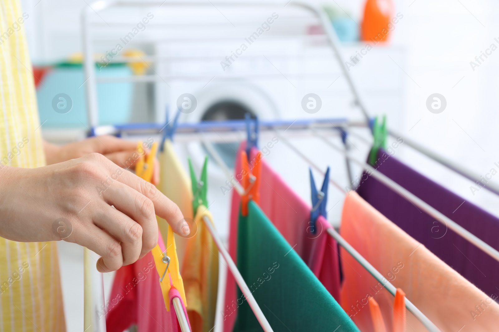 Photo of Woman hanging clean laundry on drying rack indoors, closeup