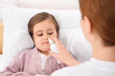 Mother using nasal spray to treat her little daughter on bed