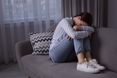 Photo of Unhappy young woman on sofa at home, space for text. Loneliness concept