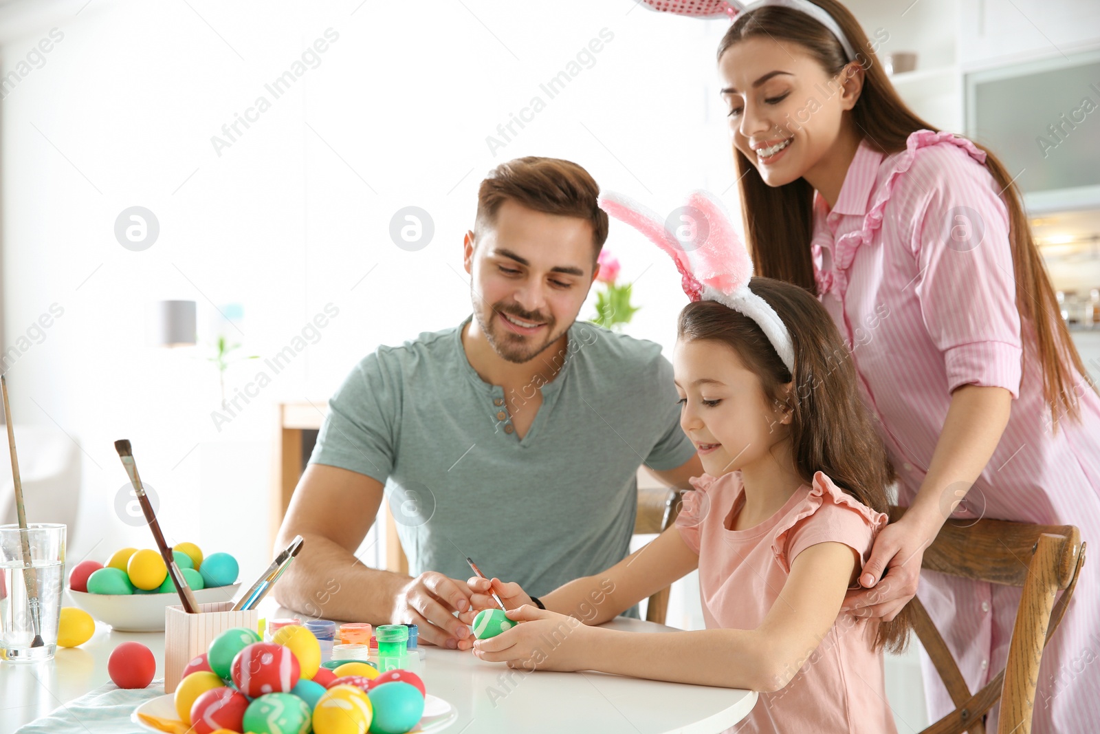 Photo of Father, mother and daughter painting Easter eggs in kitchen, space for text