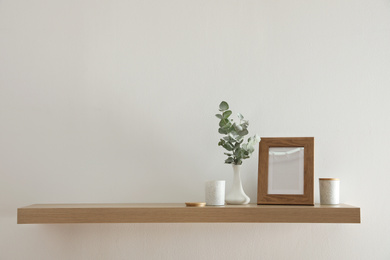 Wooden shelf with photo frame and decorative elements on light wall