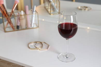 Glass of red wine and jewelry on white table indoors, space for text