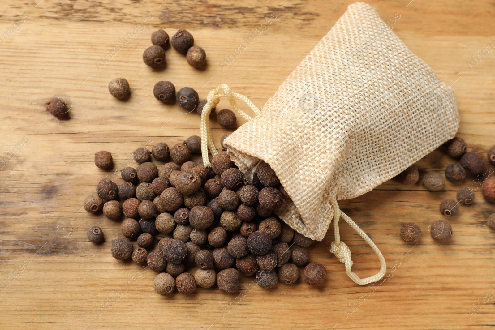 Photo of Aromatic allspice pepper grains and sack on wooden table, top view