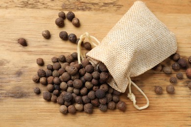 Photo of Aromatic allspice pepper grains and sack on wooden table, top view