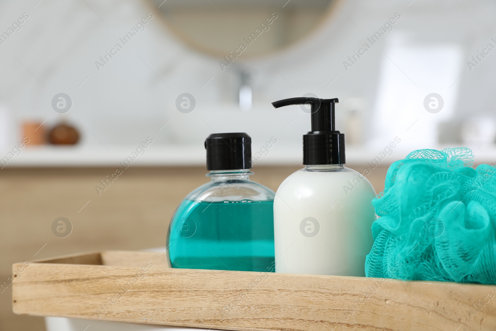 Photo of Wooden tray with bottles of shower gels and mesh pouf indoors, closeup