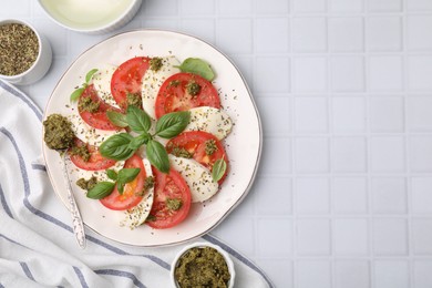 Plate of delicious Caprese salad with pesto sauce on white tiled table, flat lay. Space for text