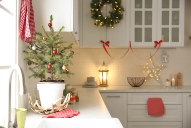 Small Christmas tree decorated with baubles and festive lights in kitchen. Space for text