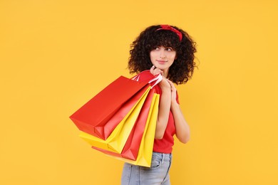 Happy young woman with shopping bags on yellow background