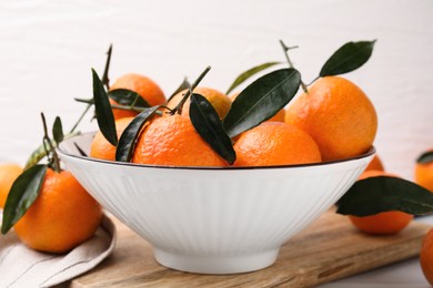 Photo of Fresh ripe tangerines with green leaves in bowl on table, closeup