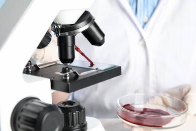 Scientist dripping blood sample onto slide on microscope in laboratory, closeup. Virus research