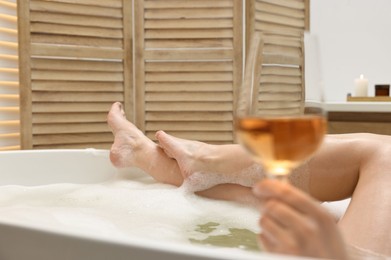 Photo of Woman with glass of wine taking bath in tub indoors, closeup