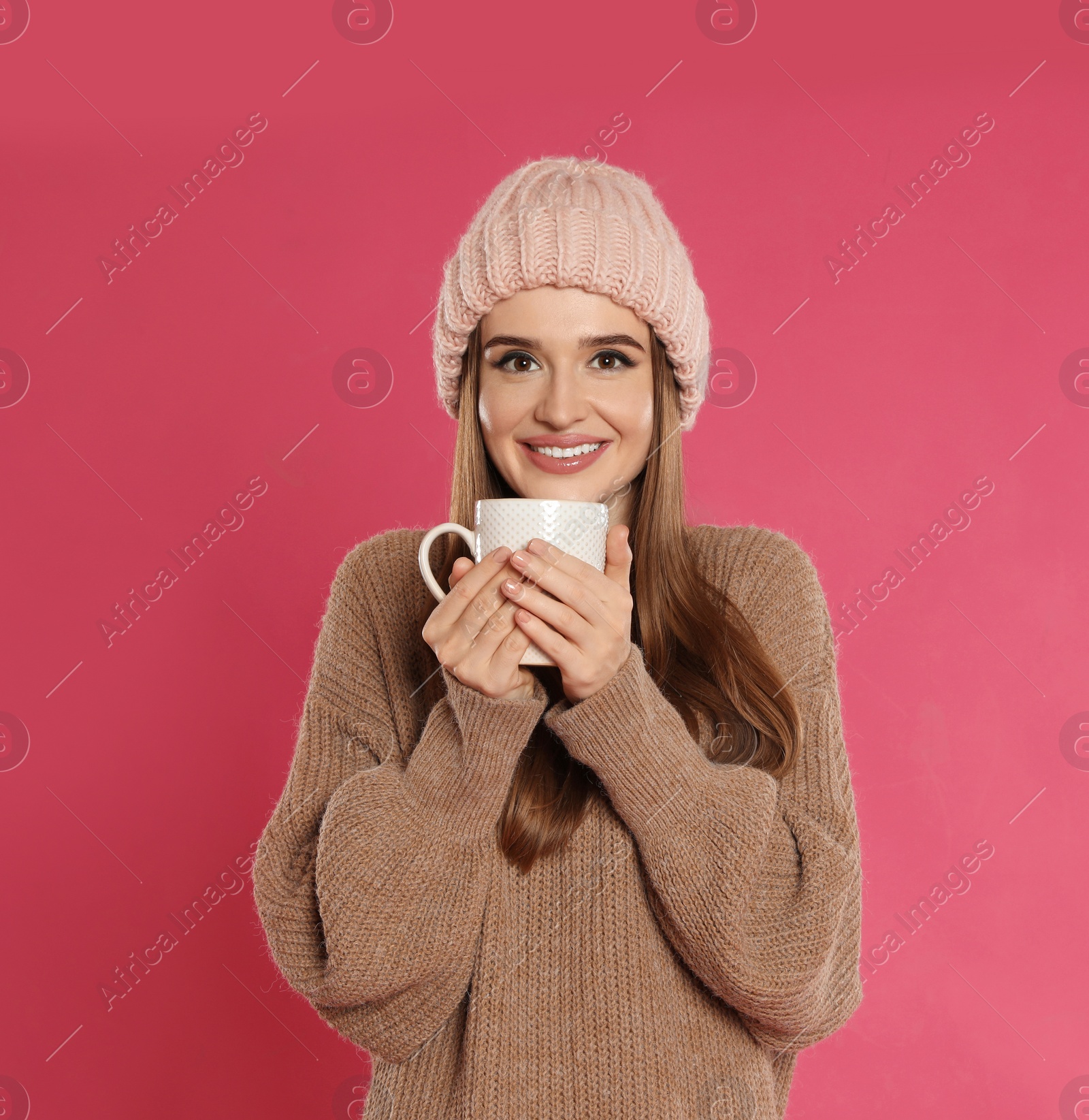 Photo of Beautiful young woman in hat and sweater with drink on pink background. Winter season