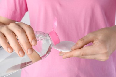 Photo of Woman pouring micellar water from bottle on cotton pad, closeup