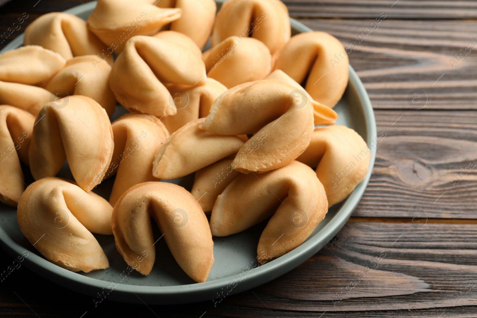 Photo of Tasty fortune cookies with predictions in plate on wooden table, closeup