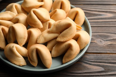 Photo of Tasty fortune cookies with predictions in plate on wooden table, closeup