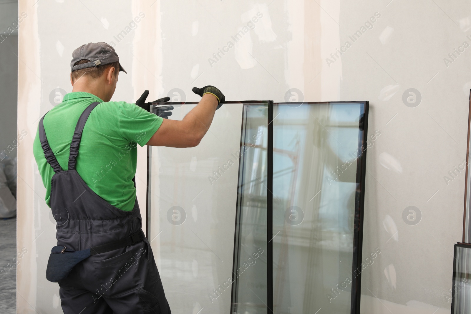 Photo of Worker in uniform preparing double glazing window for installation indoors, back view