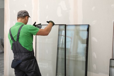 Worker in uniform preparing double glazing window for installation indoors, back view