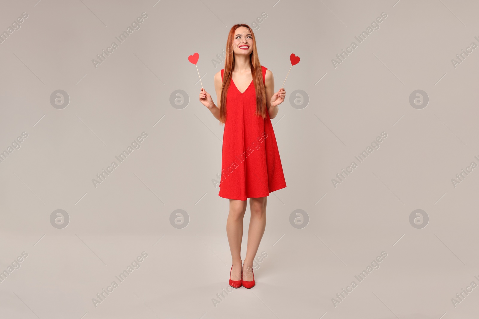 Photo of Young woman in red dress with paper hearts on light grey background
