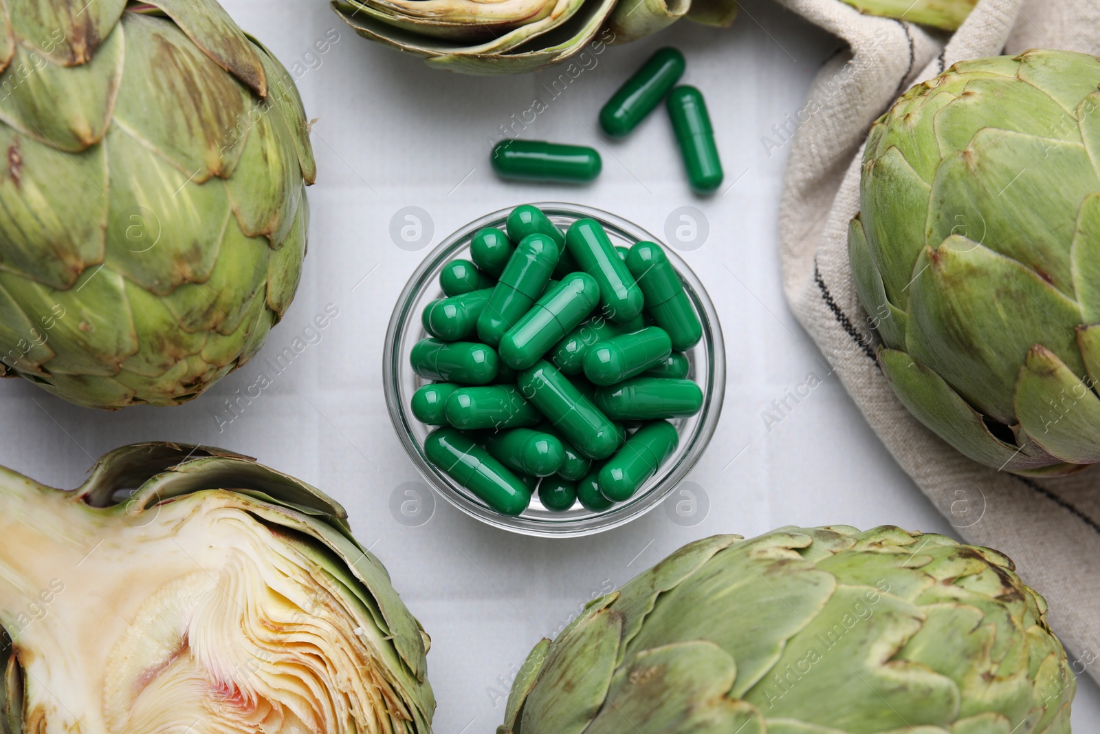Photo of Bowl with pills and fresh artichokes on white tiled table, flat lay