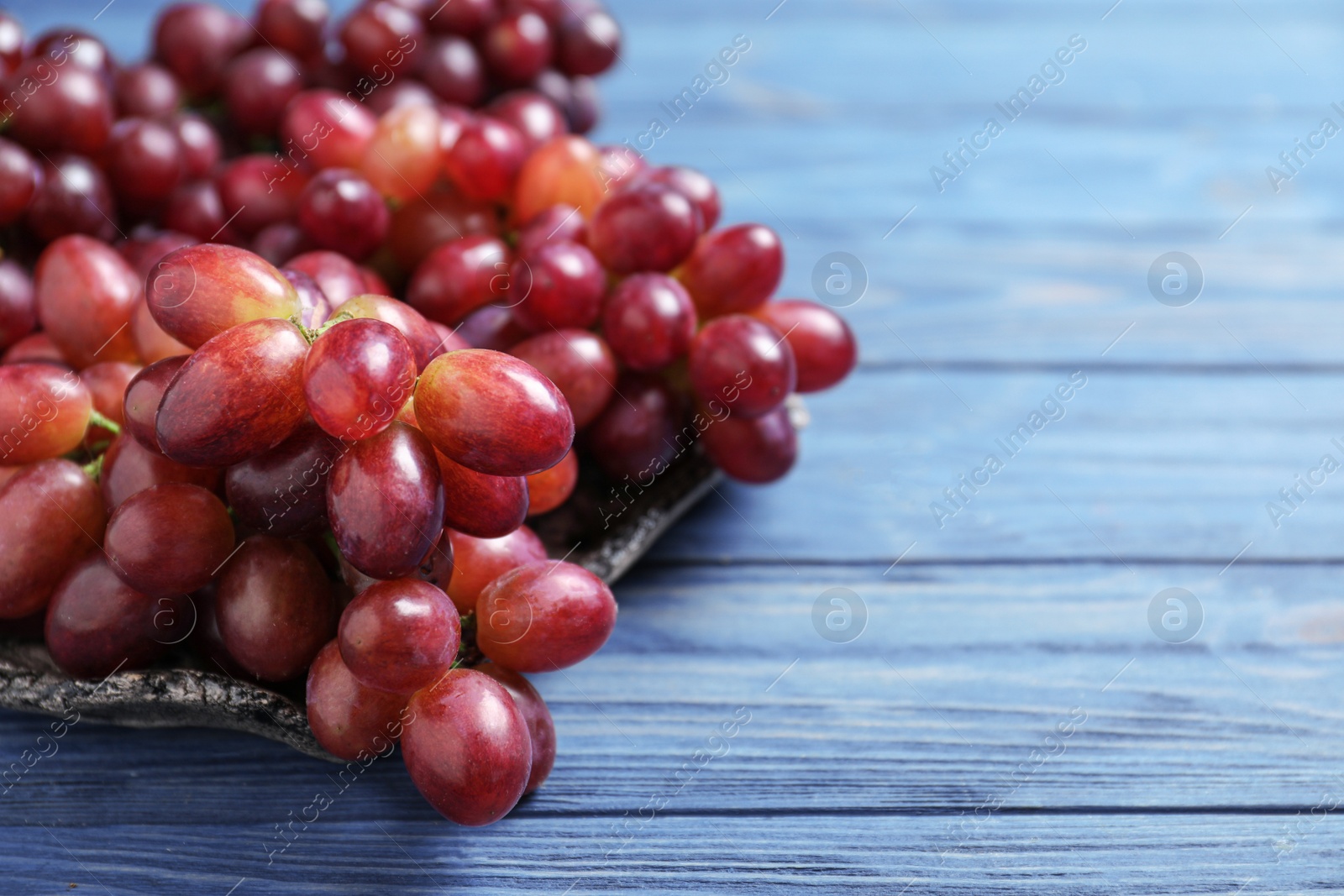 Photo of Fresh ripe juicy grapes on blue wooden table. Space for text