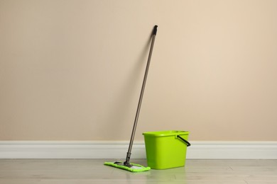 Photo of Mop and plastic bucket on floor near beige wall. Cleaning service