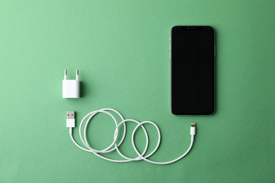 Smartphone and USB charger on green background, flat lay. Modern technology