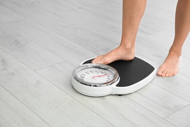 Photo of Woman stepping on floor scales indoors, space for text. Overweight problem