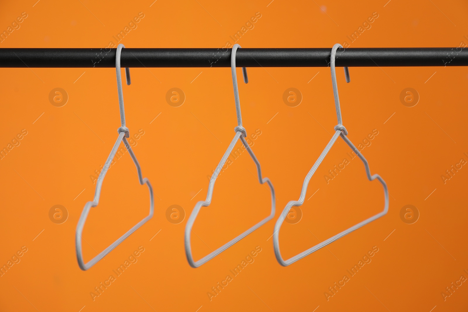 Photo of Empty clothes hangers on rack against orange background