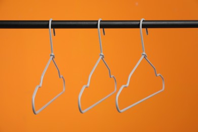 Photo of Empty clothes hangers on rack against orange background