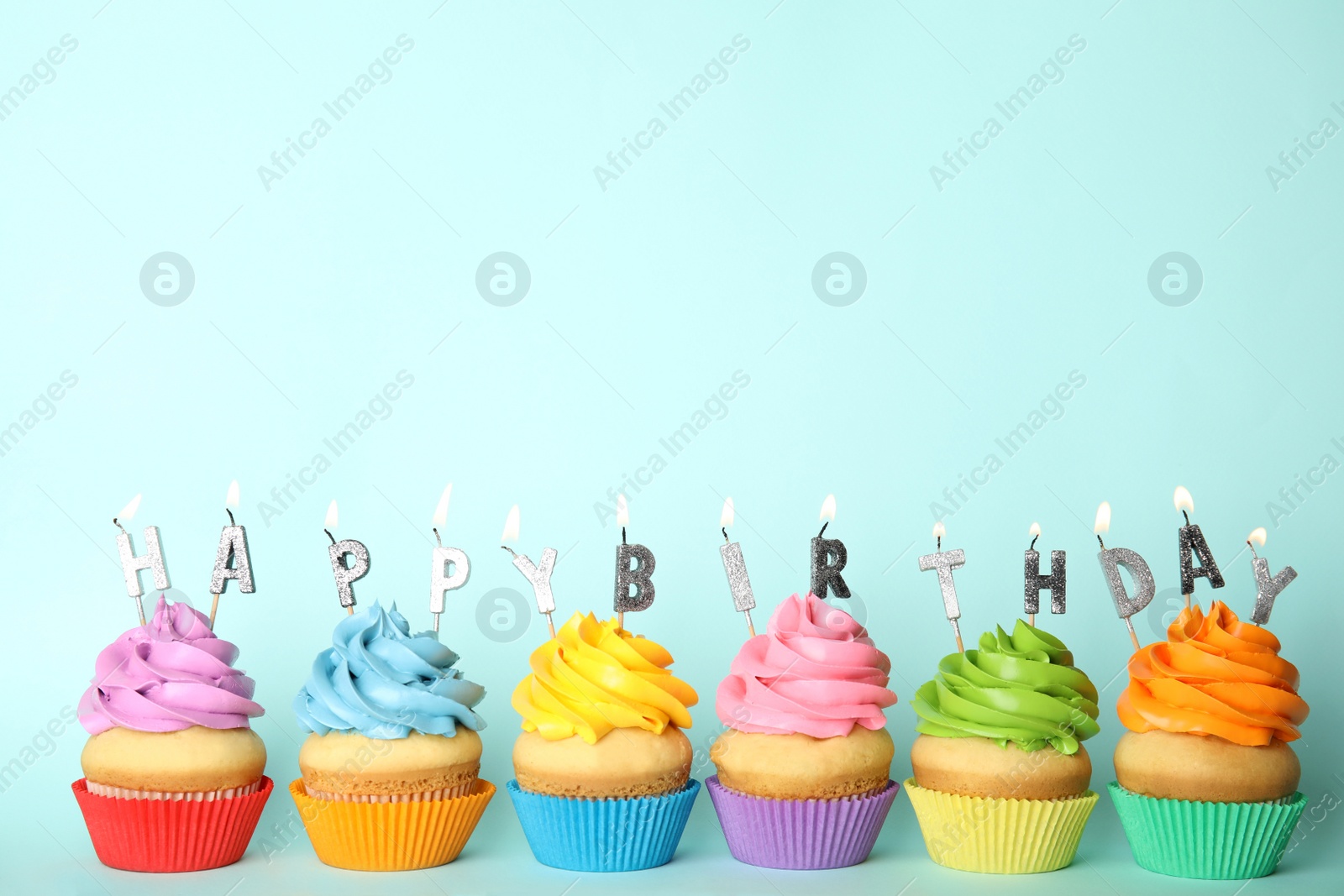 Photo of Birthday cupcakes with burning candles on light blue background. Space for text