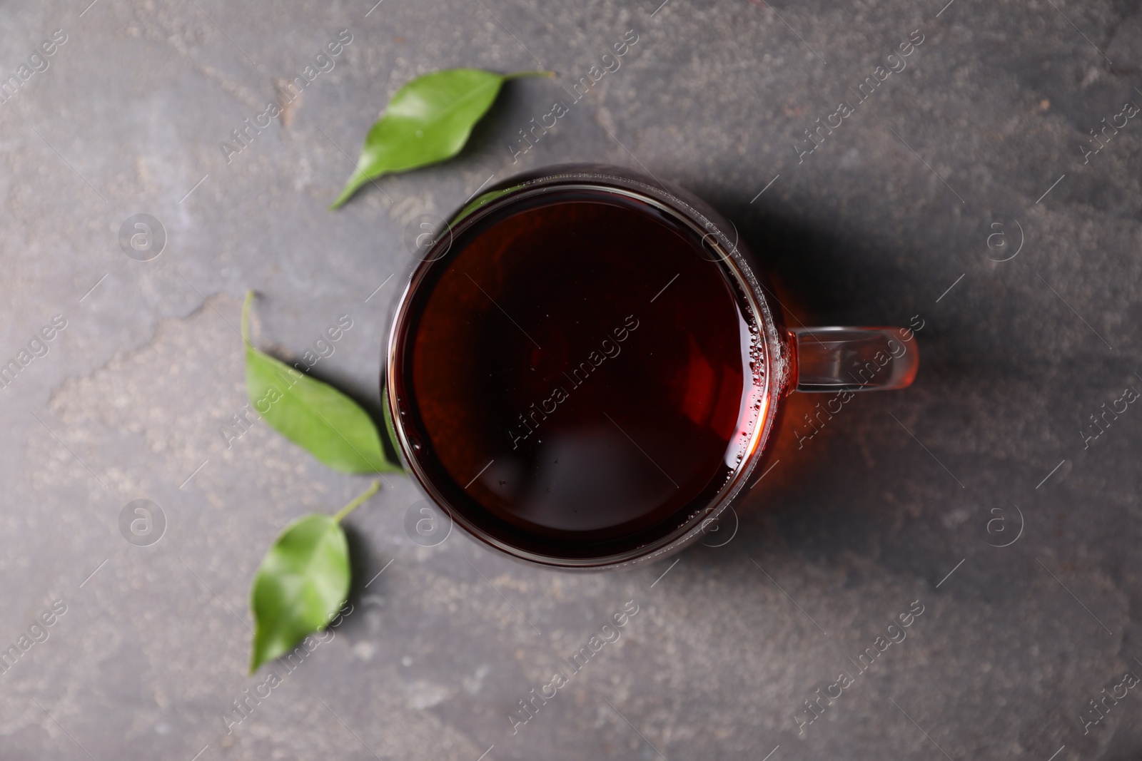 Photo of Tasty hot tea in cup and leaves on grey table, top view