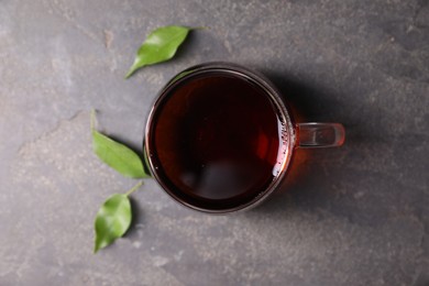 Photo of Tasty hot tea in cup and leaves on grey table, top view