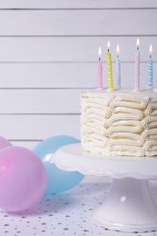 Delicious cake with burning candles and festive decor on white table, closeup