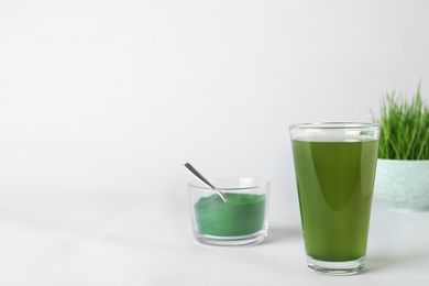 Photo of Glass of spirulina drink and bowl with powder on white background. Space for text