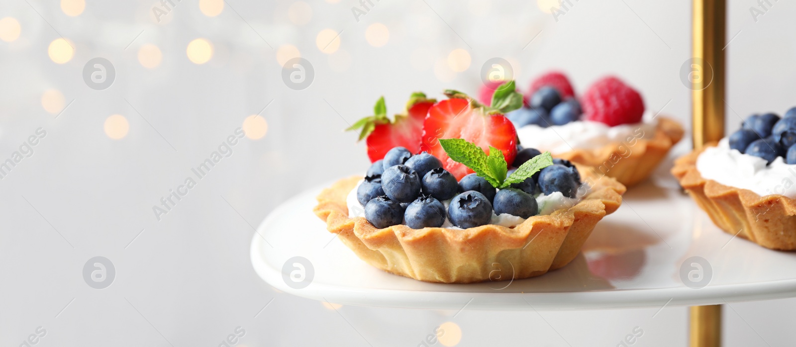 Image of Tarts with different berries on cake stand, space for text. Banner design