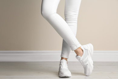 Photo of Woman wearing stylish sneakers near beige wall indoors, closeup