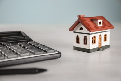 Photo of Calculator, house model and pen on light table. Real estate agent's workplace