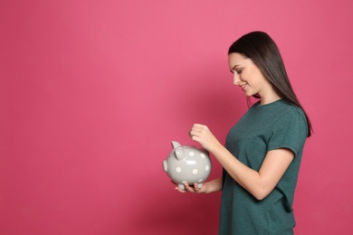 Young woman putting coin into piggy bank on color background. Space for text