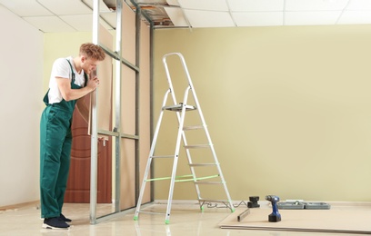 Young worker installing drywall indoors. Home repair service