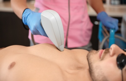 Photo of Young man undergoing laser epilation procedure in beauty salon