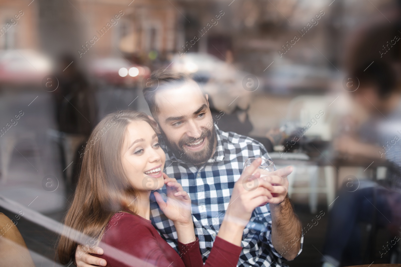 Photo of Lovely young couple spending time together in cafe, view from outdoors through window