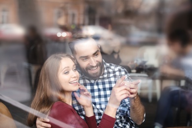 Photo of Lovely young couple spending time together in cafe, view from outdoors through window