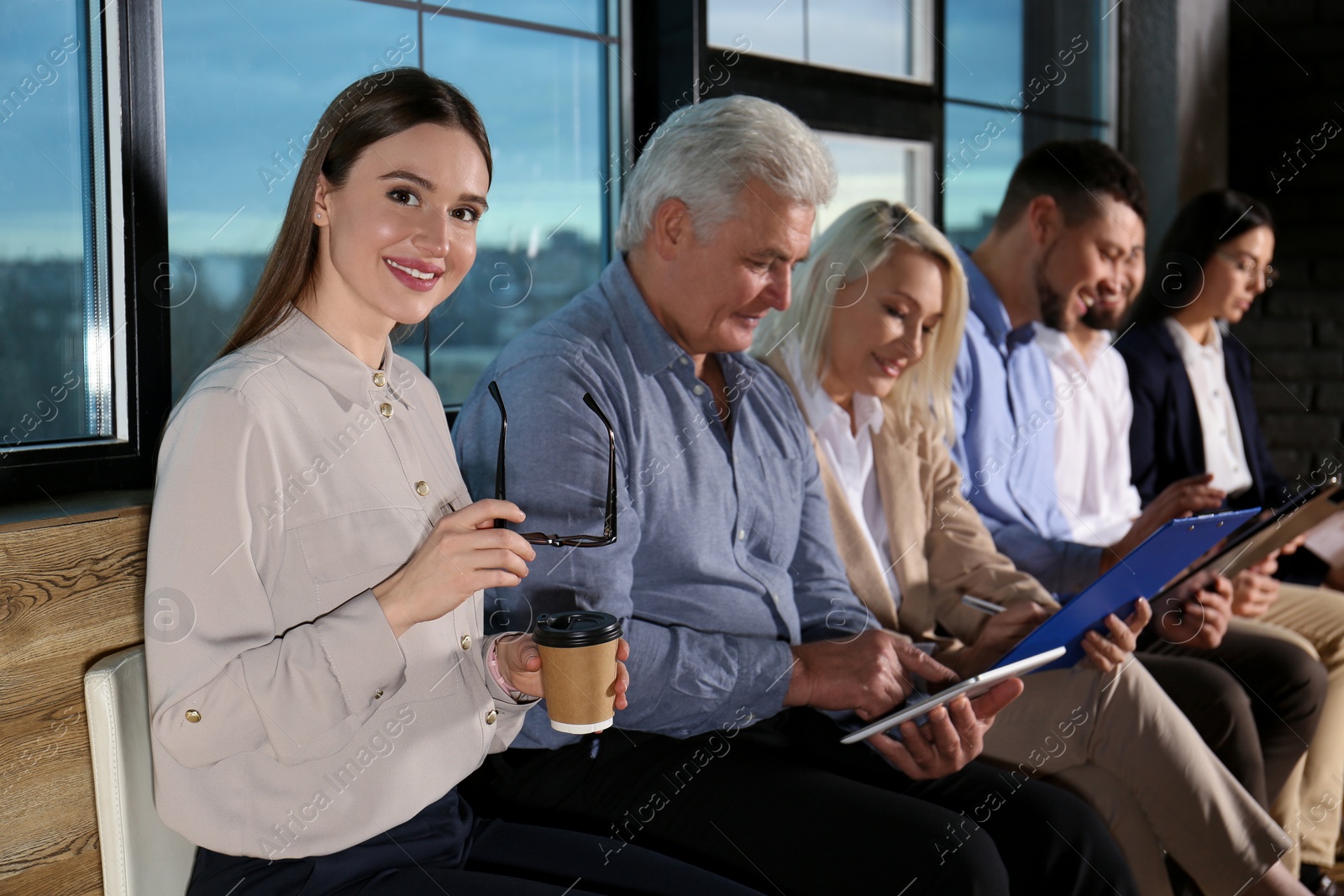 Photo of Young woman with eyeglasses and cup of coffee waiting for job interview in office hall