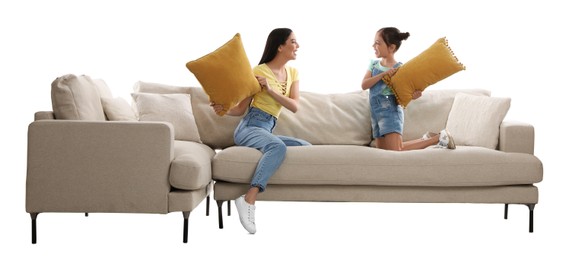 Young woman and her daughter having pillow fight on comfortable sofa against white background