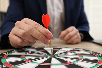 Business targeting concept. Man with dart aiming at dartboard at table, closeup