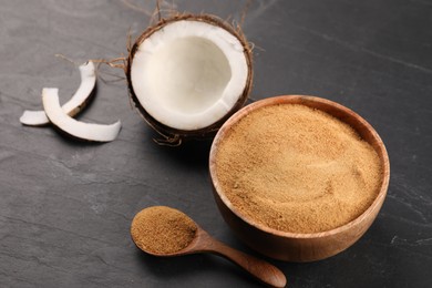 Photo of Spoon with coconut sugar, bowl and fruit on dark textured table, closeup