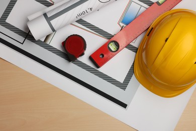 Photo of Construction drawings, safety hat, tape measure and bubble level on wooden table, top view