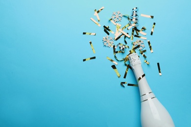Photo of Bottle with champagne and shiny confetti on light blue background, flat lay. Space for text